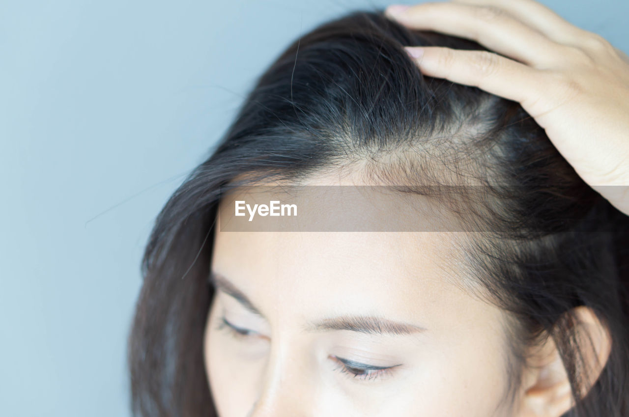 Close-up of woman showing scalp over colored background