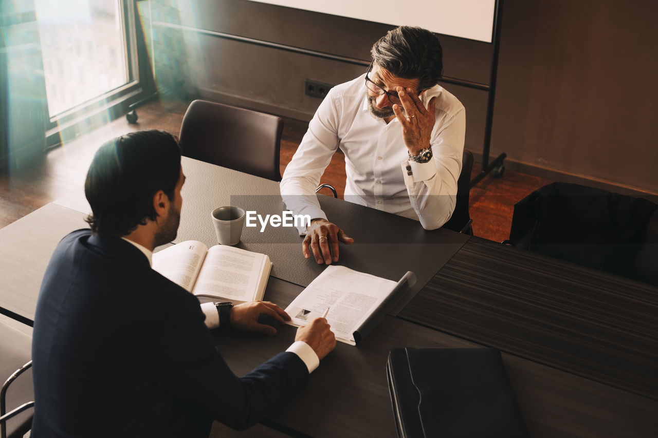 High angle view of male lawyer showing file to mature stressed client at board room in law office