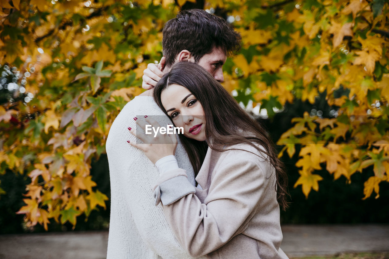 Smiling woman embracing partner while standing against tree