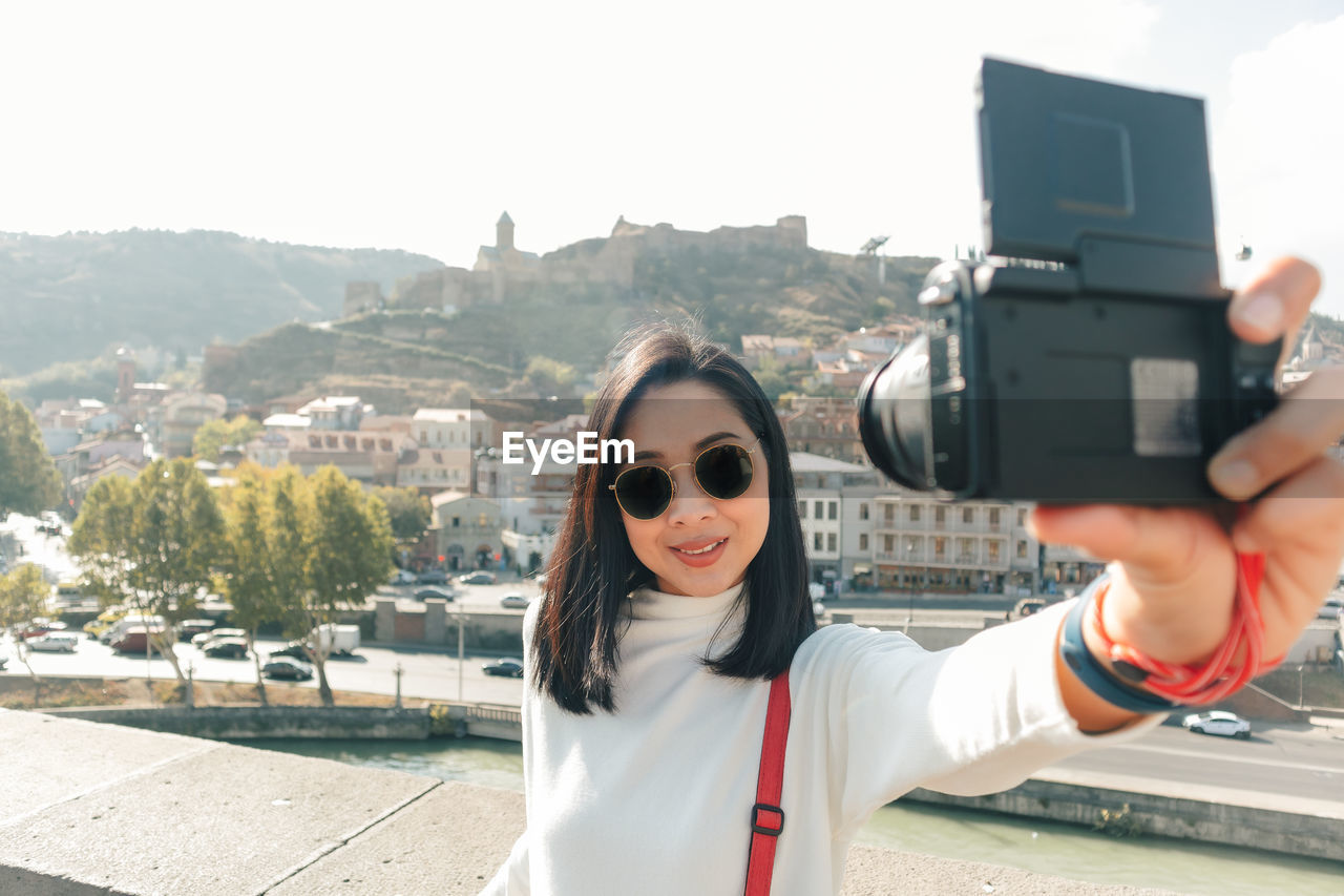 Asian woman tourist is taking selfie of herself and the view of tbilisi old town in georgia.