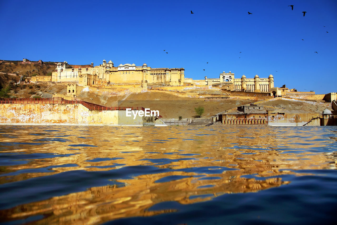 Amer fort by river against clear blue sky