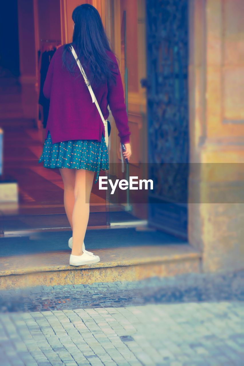 Rear view of woman wearing skirt holding cell phone standing at doorway