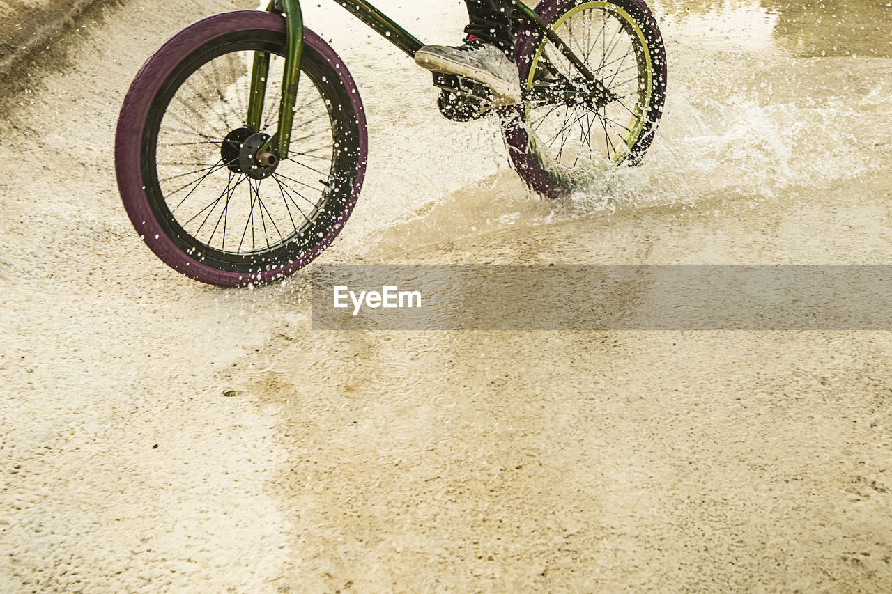 Low section of person riding bicycle in puddle