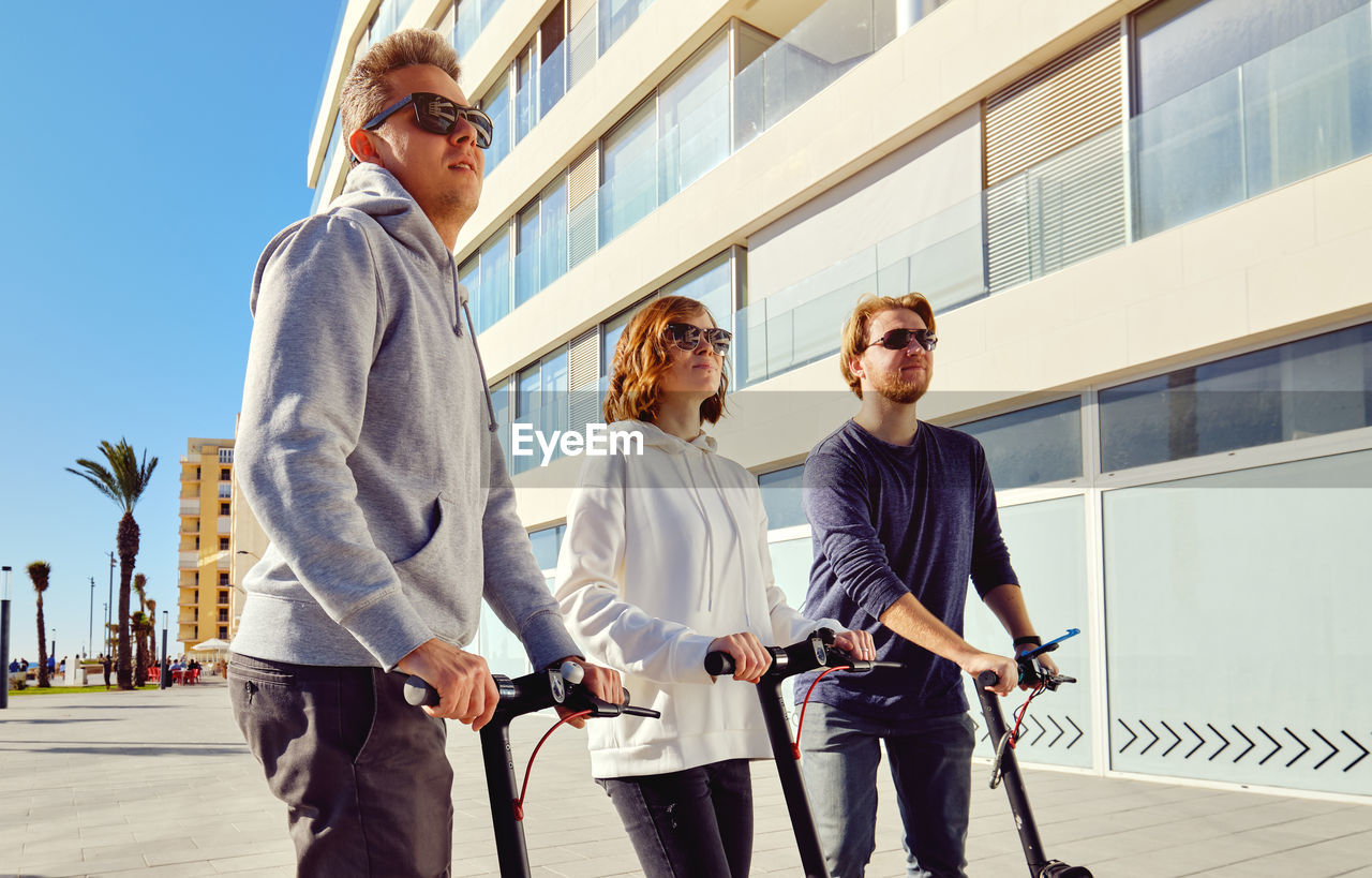 Friends using push scooters in city on sunny day