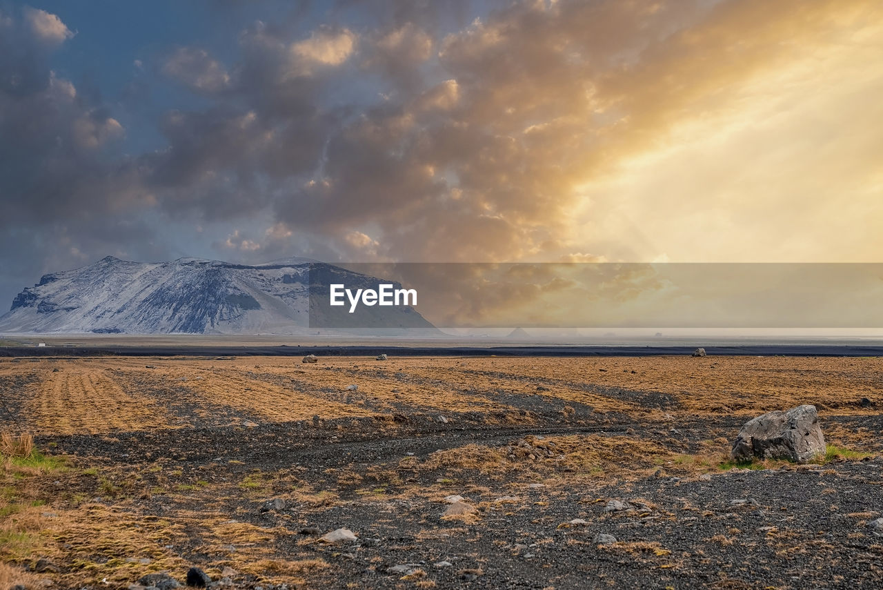View of mountain on lava sand in highland against cloudy sky during sunset
