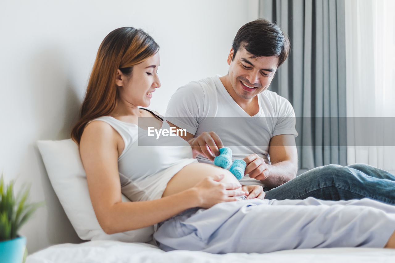 Smiling man holding booties on pregnant mother stomach at home