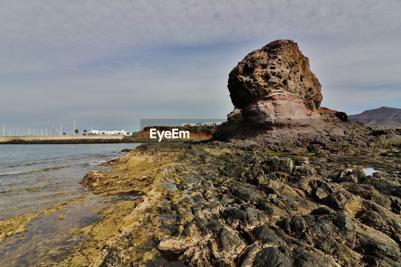 Rock formations in sea against cloudy sky