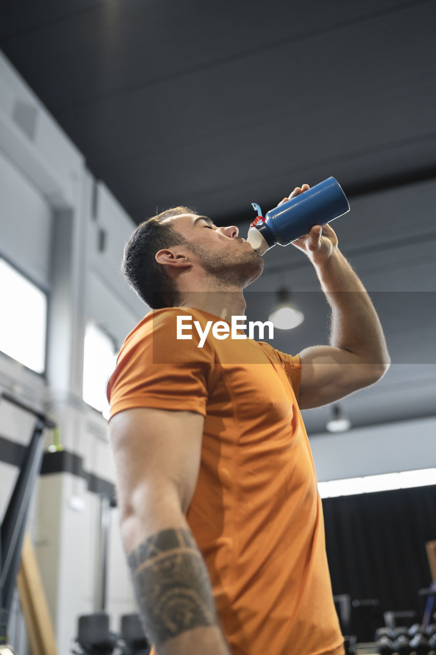 Thirsty man drinking water while standing in gym