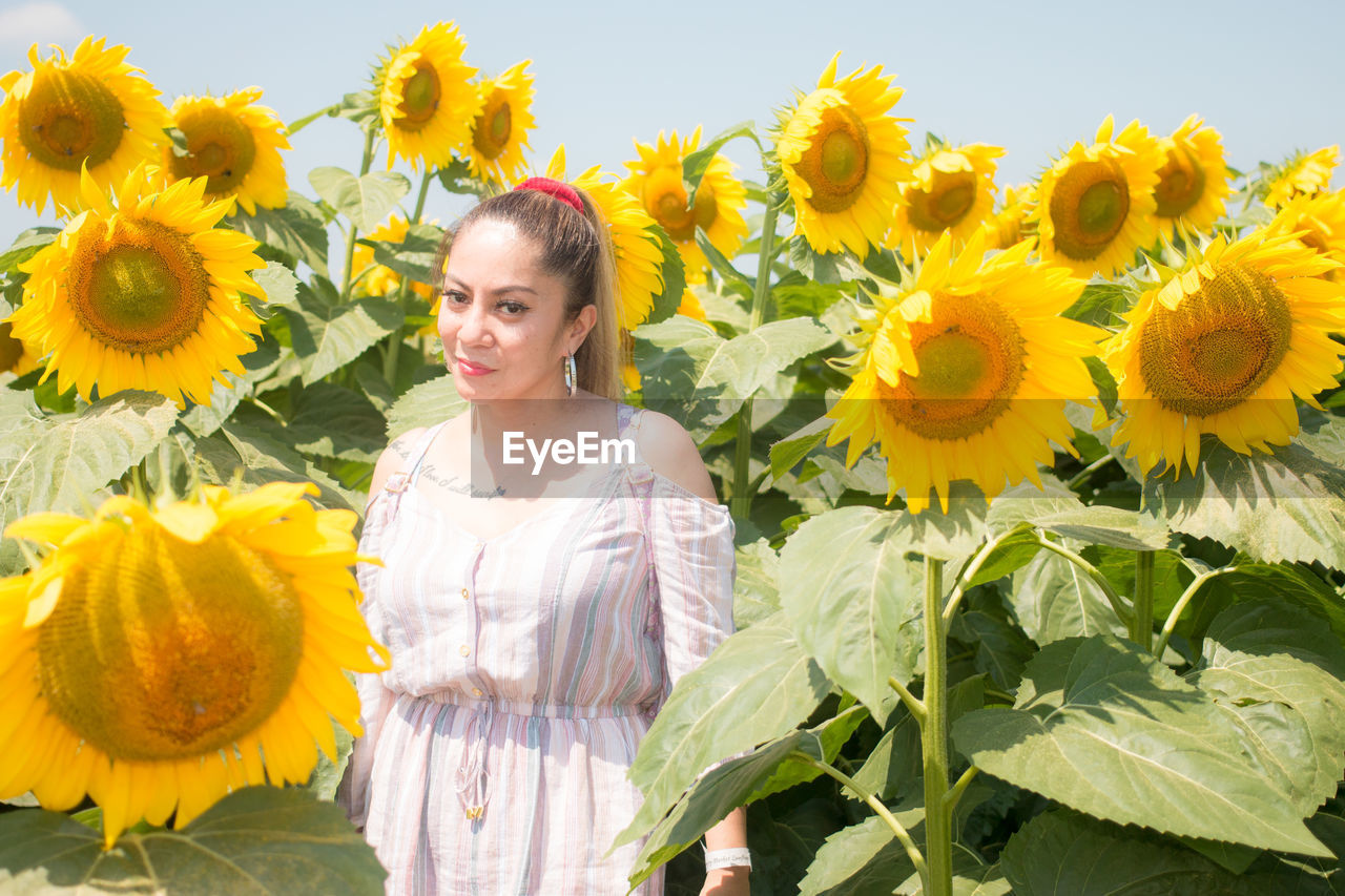 PORTRAIT OF SMILING WOMAN STANDING AGAINST SUNFLOWER