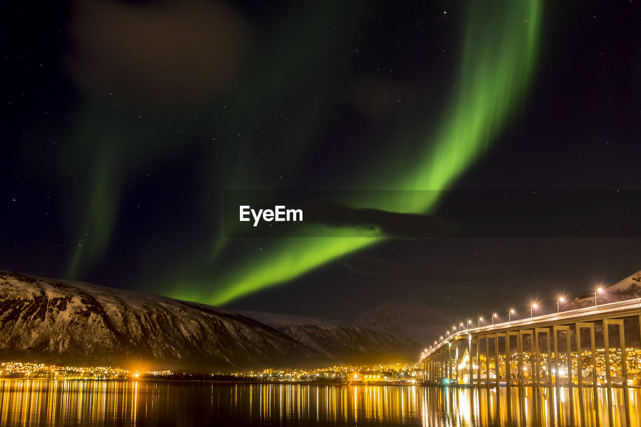 Illuminated bridge over river against aurora borealis