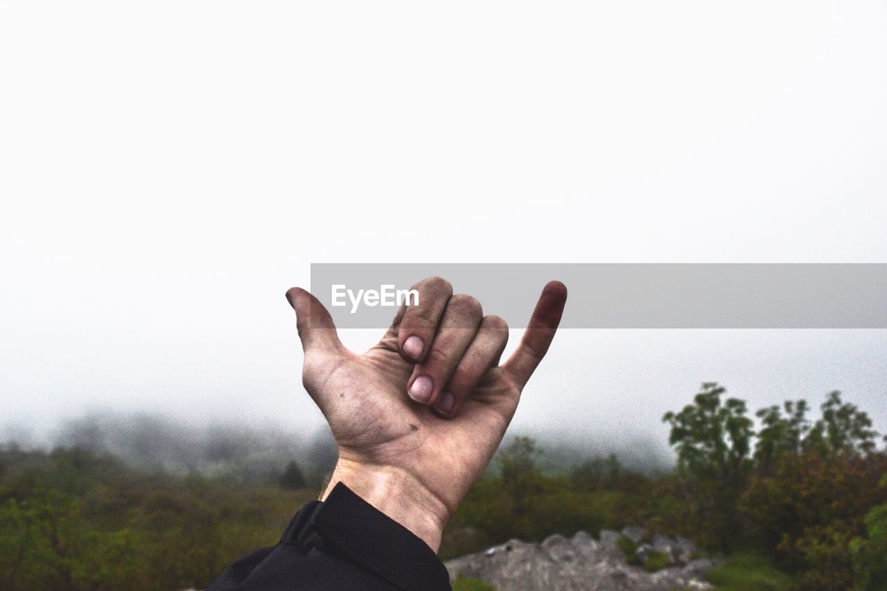 Cropped image of hand showing shaka sign on field against sky