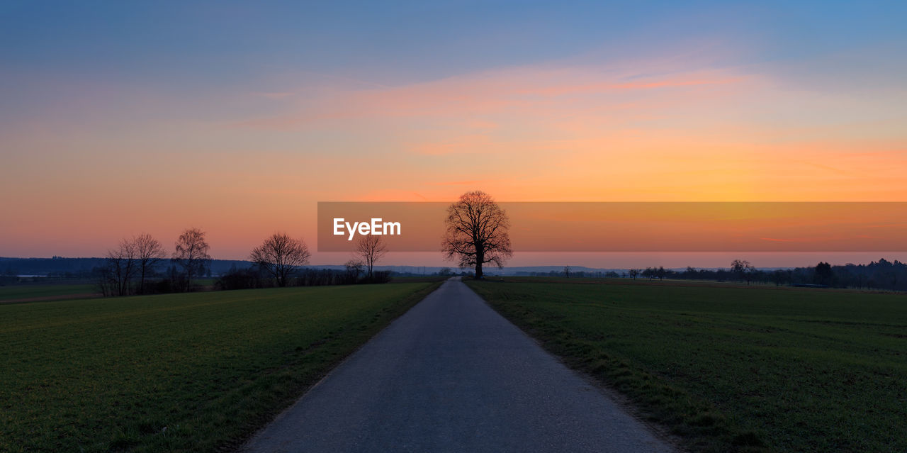 Road amidst field against sky during sunset