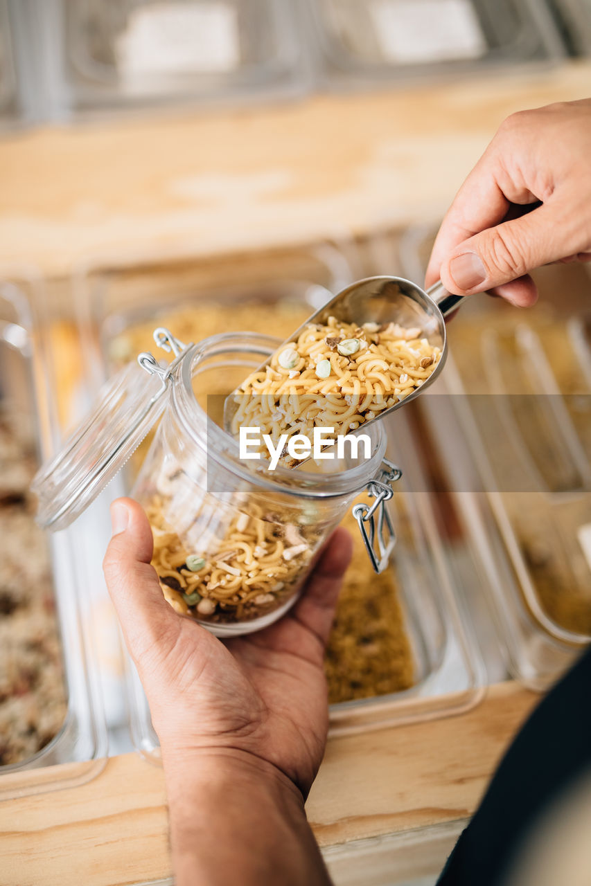 Back view of anonymous female pouring dry pasta inside glass jar in local store