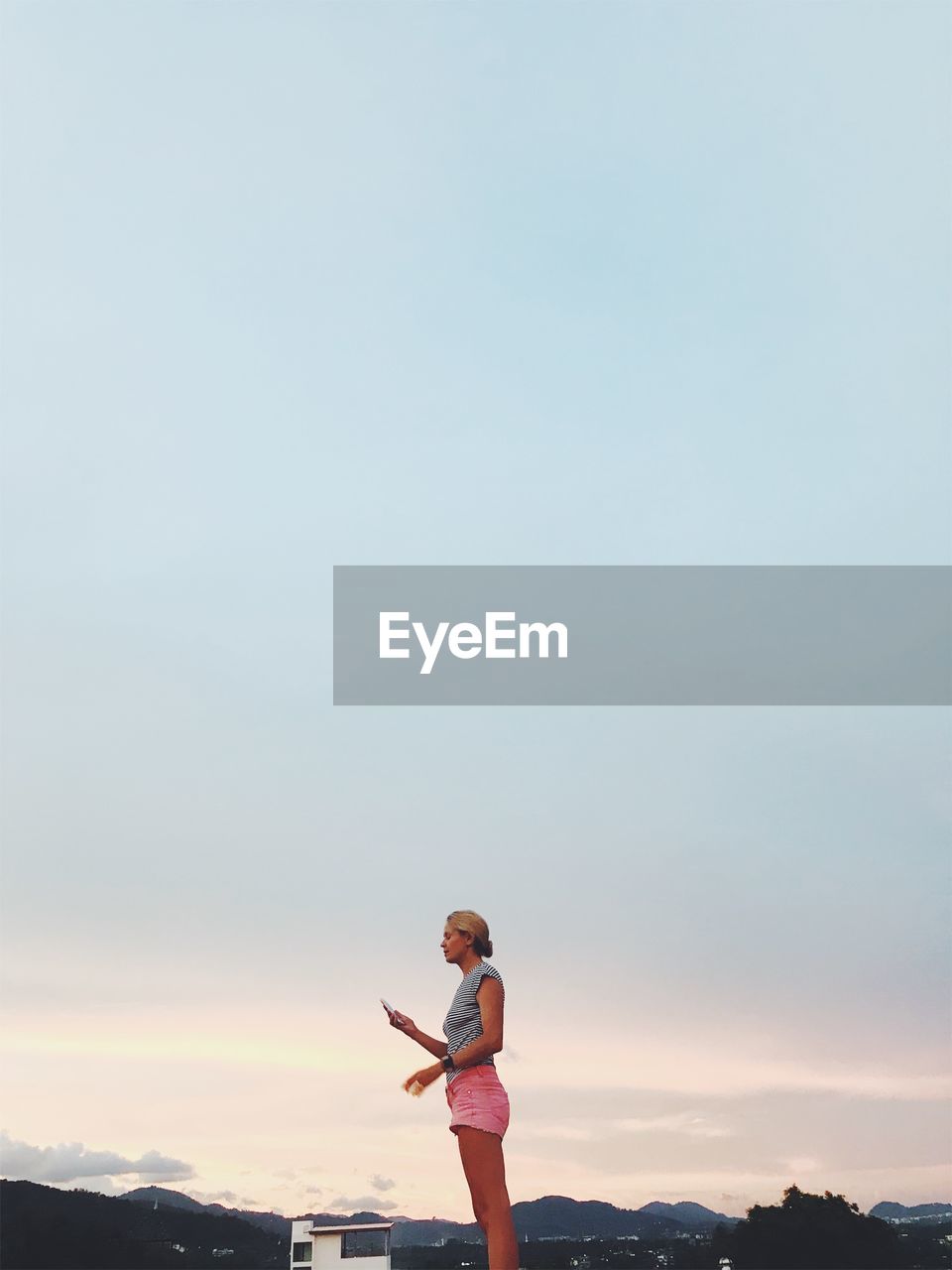 Side view of woman standing against cloudy sky during sunset