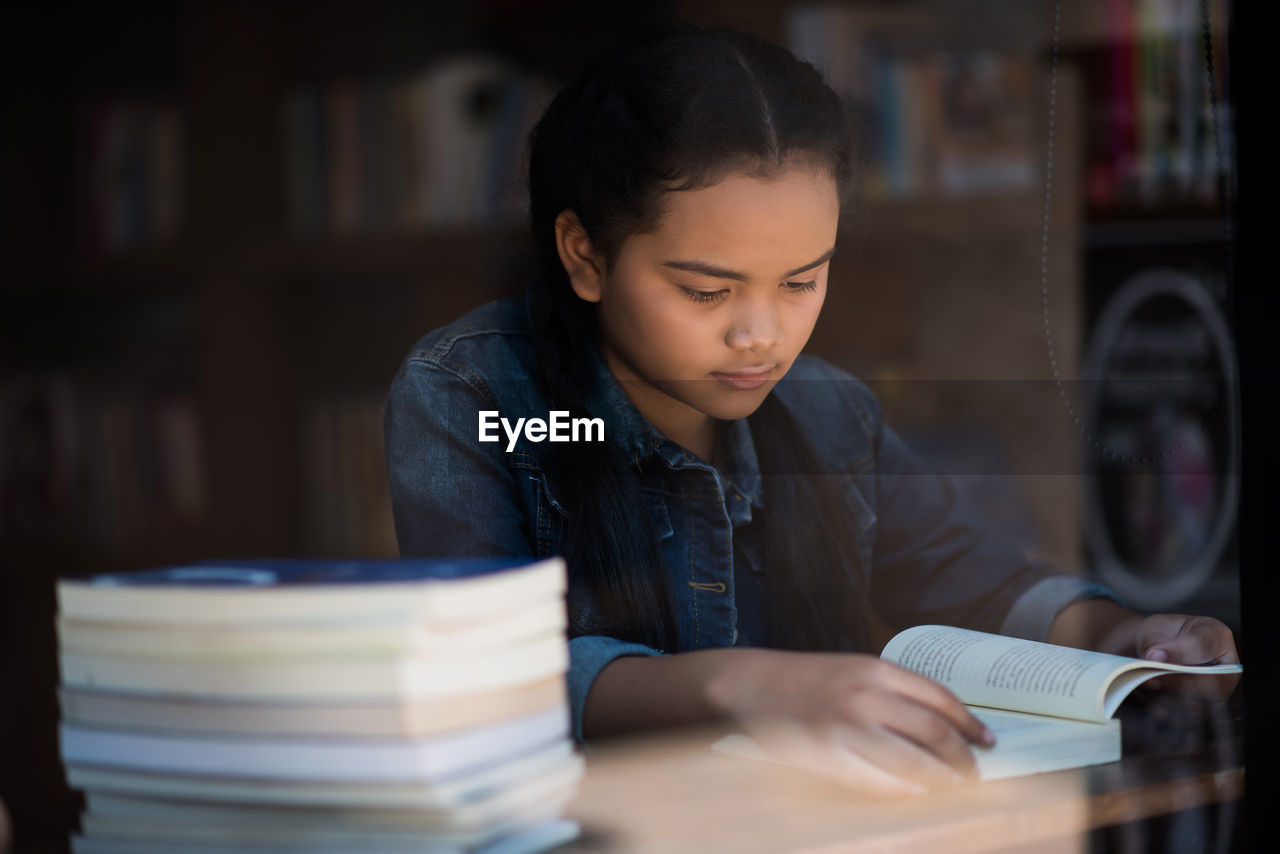 Girl reading book while sitting at table