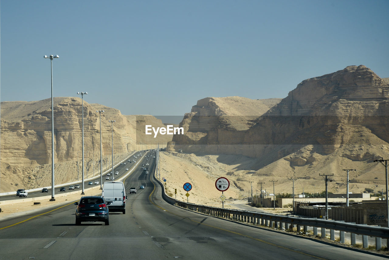 VEHICLES ON ROAD AGAINST MOUNTAINS