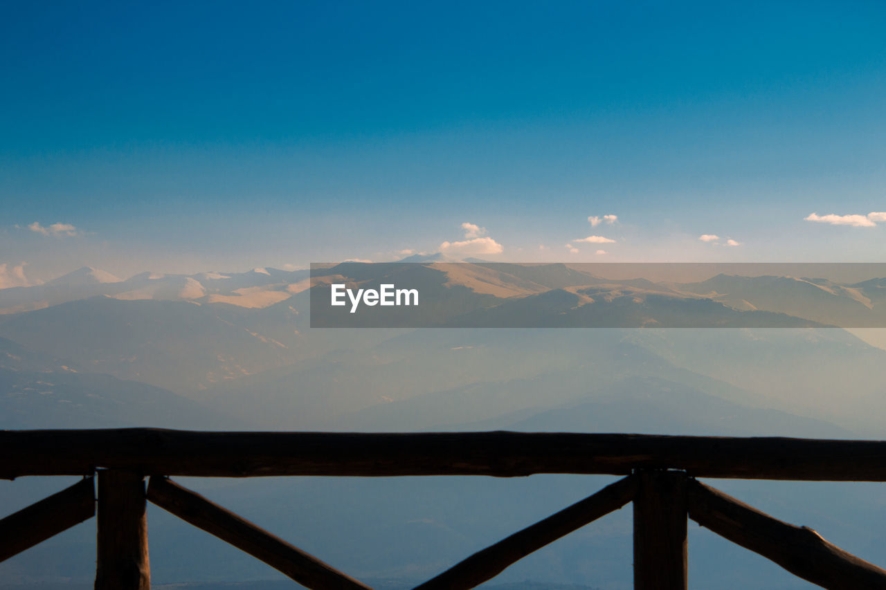 sky, horizon, mountain, scenics - nature, morning, sunrise, beauty in nature, dawn, nature, environment, landscape, mountain range, tranquility, sunlight, reflection, cloud, tranquil scene, architecture, blue, water, no people, travel destinations, travel, bridge, idyllic, outdoors, fog, non-urban scene, built structure, land, tourism, lake, wood, railing, trip, holiday, day, vacation