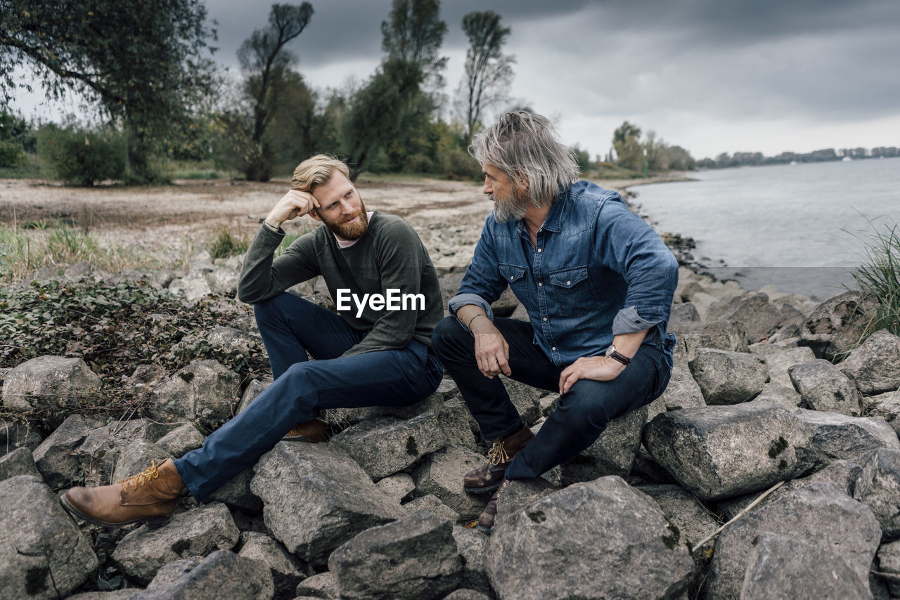 Father and son spending time together outdoors, taking a break, sitting on stones