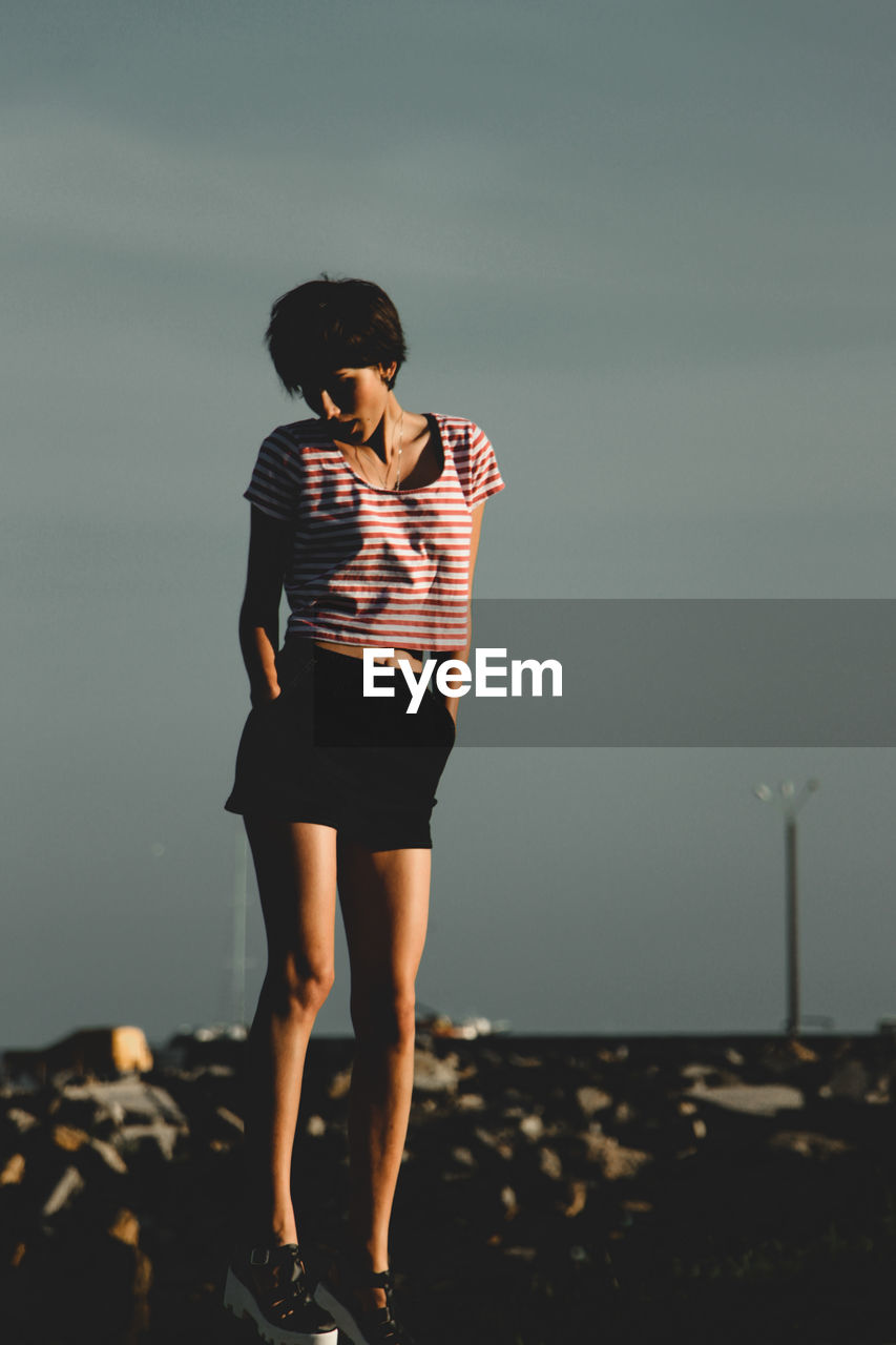 Full length of young woman standing at beach against sky during sunset