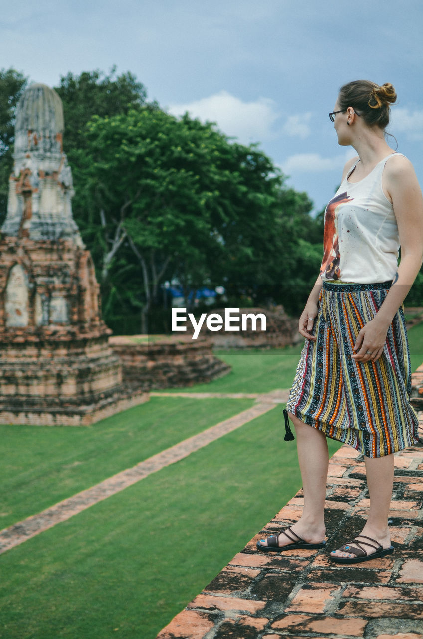 Woman looking away standing by built structure against sky