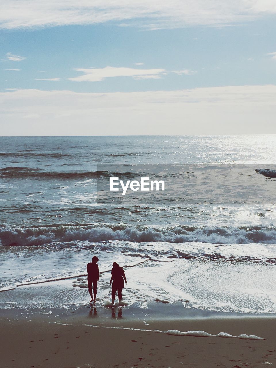 Rear view of couple walking on shore at beach against sky