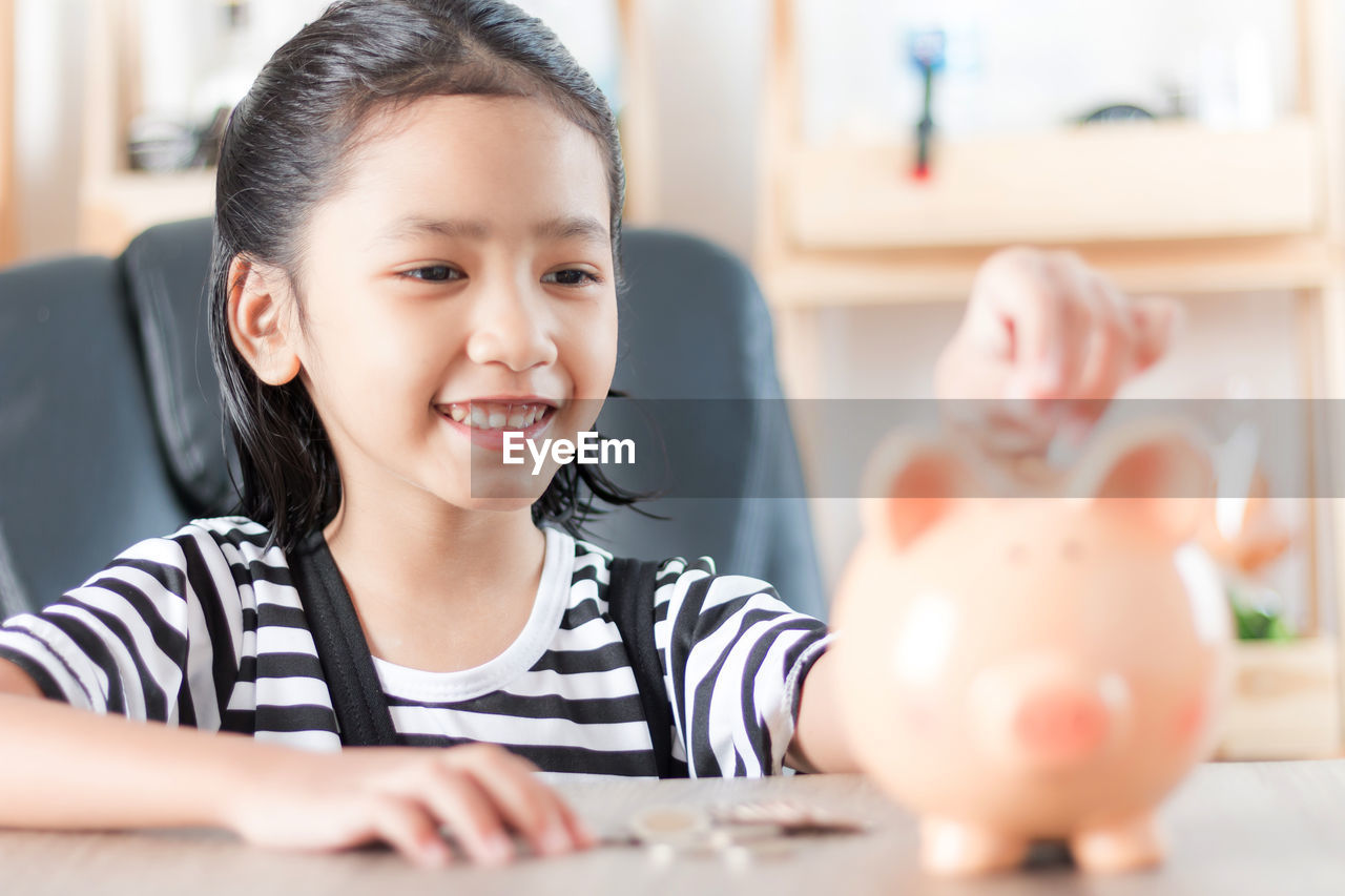 Girl putting coin in piggy bank at home