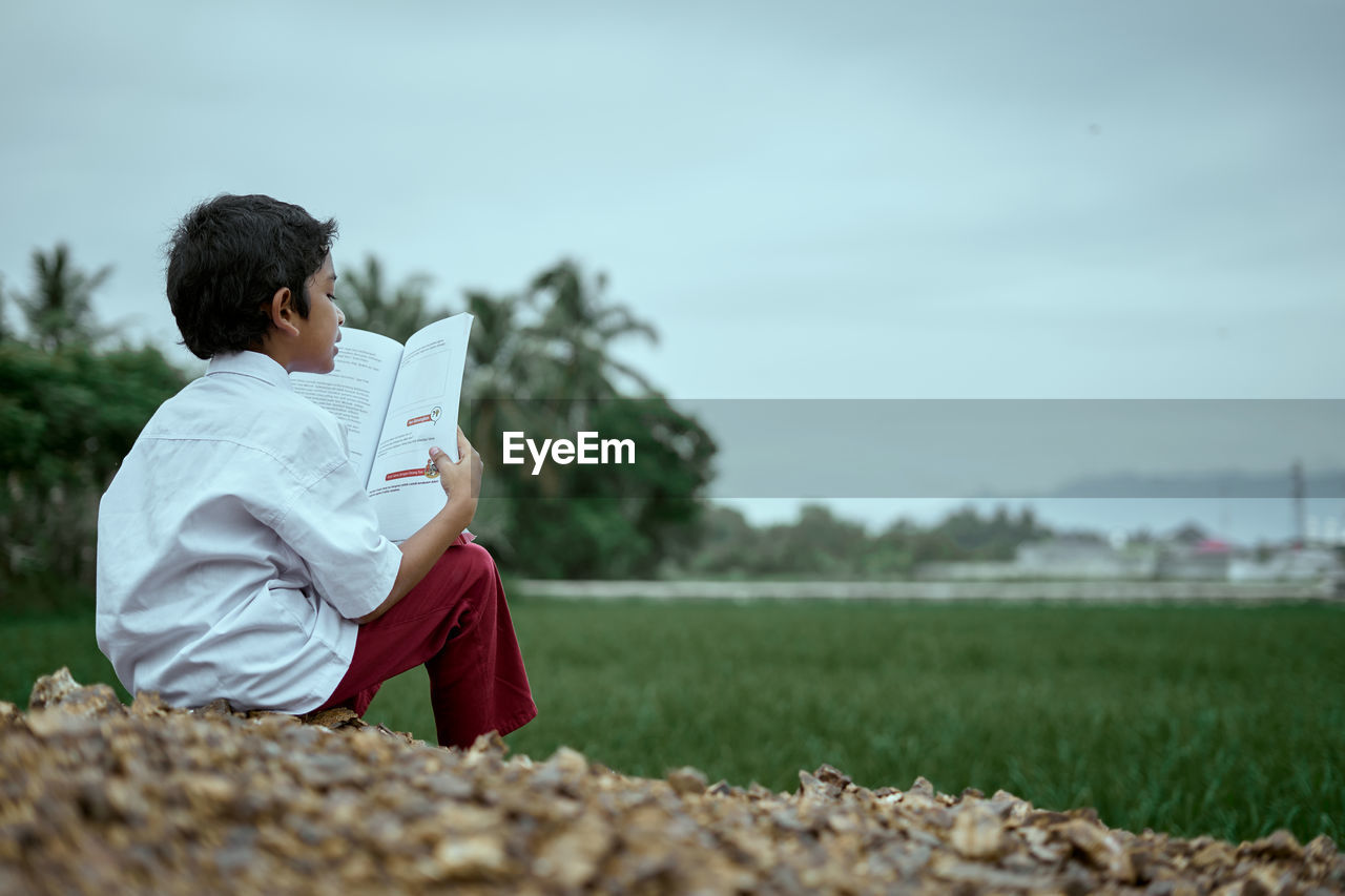 MAN SITTING ON FIELD BY LAND