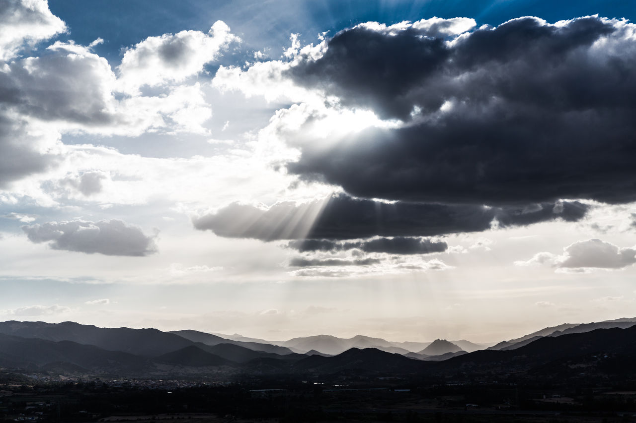 SUNLIGHT STREAMING THROUGH CLOUDS OVER SILHOUETTE MOUNTAIN