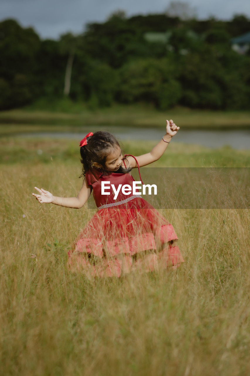 Little girl in a red dress and sun glasses playing in the grass field at midday