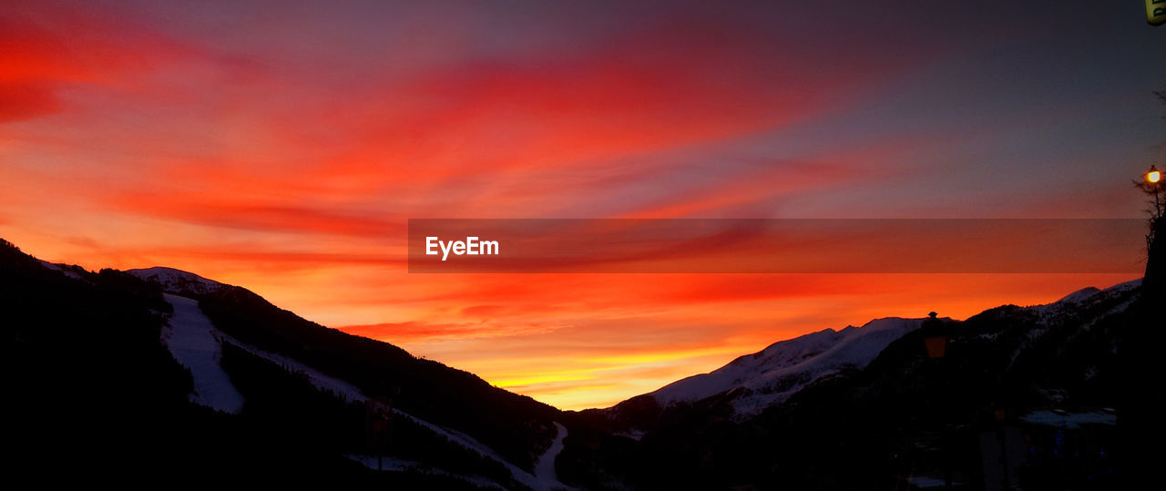 Scenic view of dramatic sky over silhouette mountains during sunset