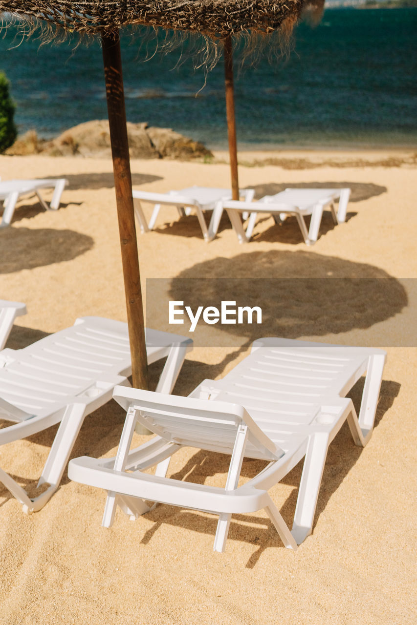 chair, beach, land, sand, water, seat, sea, relaxation, nature, holiday, vacation, trip, summer, lounge chair, tranquility, furniture, parasol, tranquil scene, sunshade, no people, deck chair, sunlight, outdoor furniture, shade, outdoor chair, beauty in nature, travel destinations, table, umbrella, absence, beach umbrella, tropical climate, scenics - nature, wood, idyllic, day, empty, travel, outdoors, coastline, sky, shadow, tourist resort, tree, horizon over water, luxury, wealth, plant, horizon, tourism, sunny, hotel