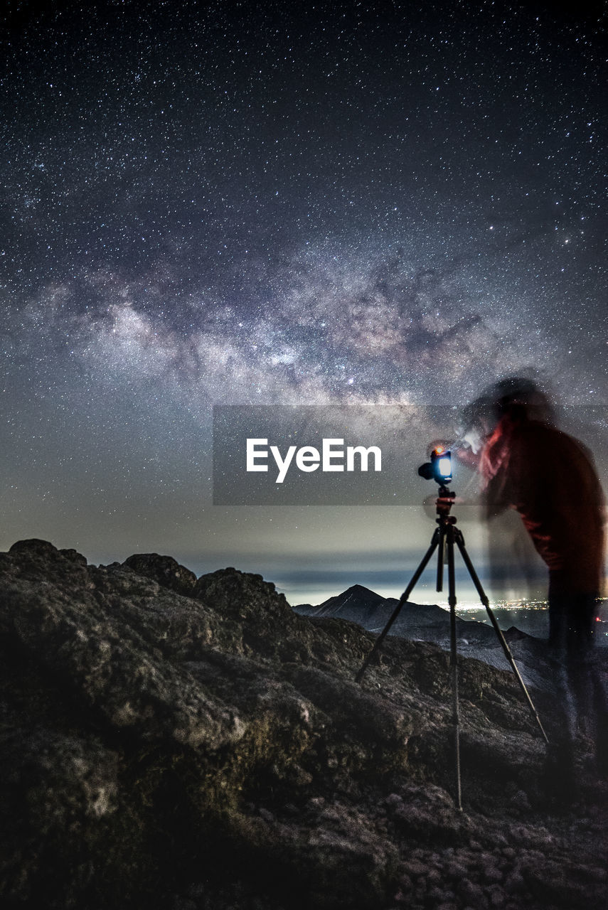 Double exposure of man photographing sky at night