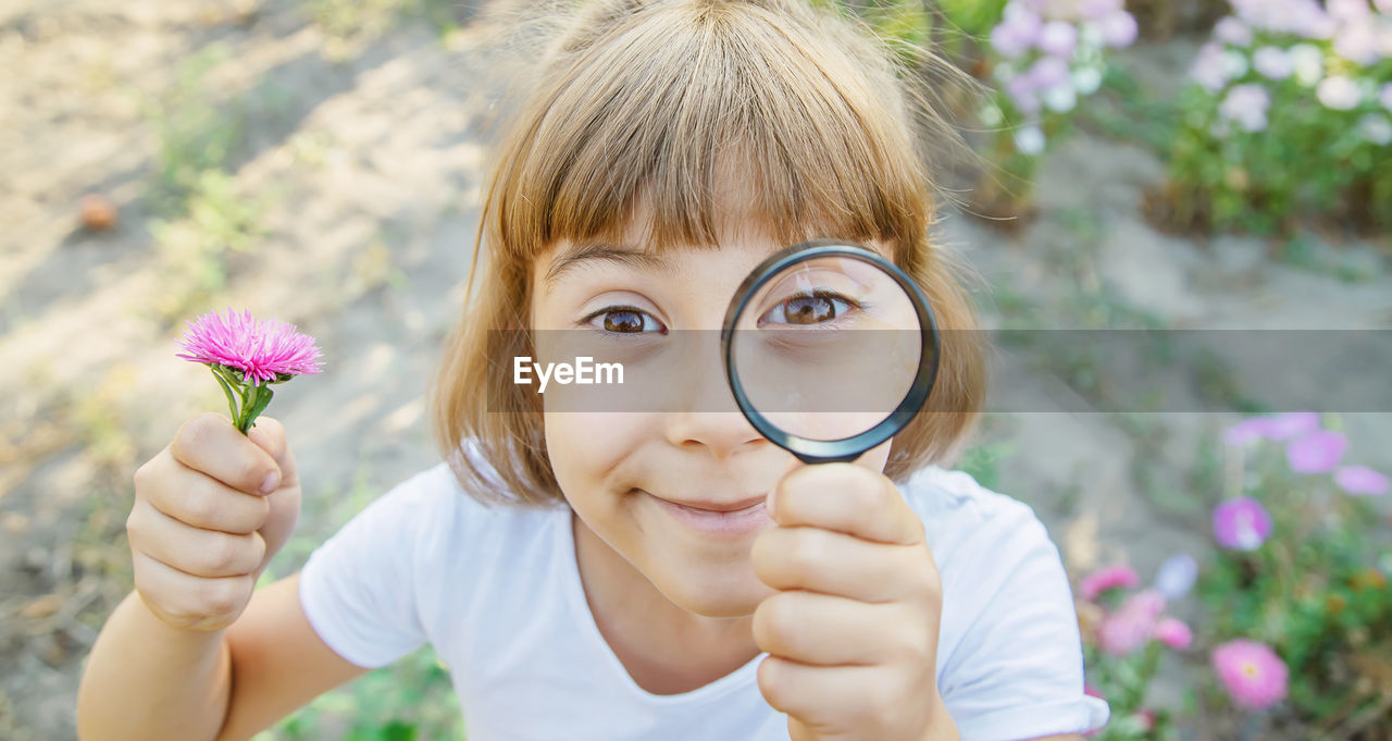 Portrait of smiling girl holding flower looking through magnifying glass