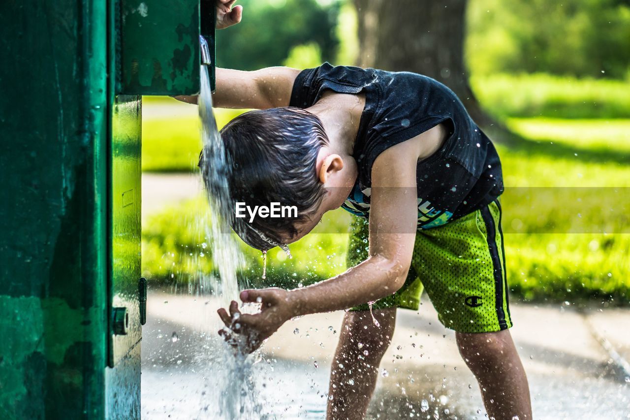 Boy washing hair from faucet at park during summer