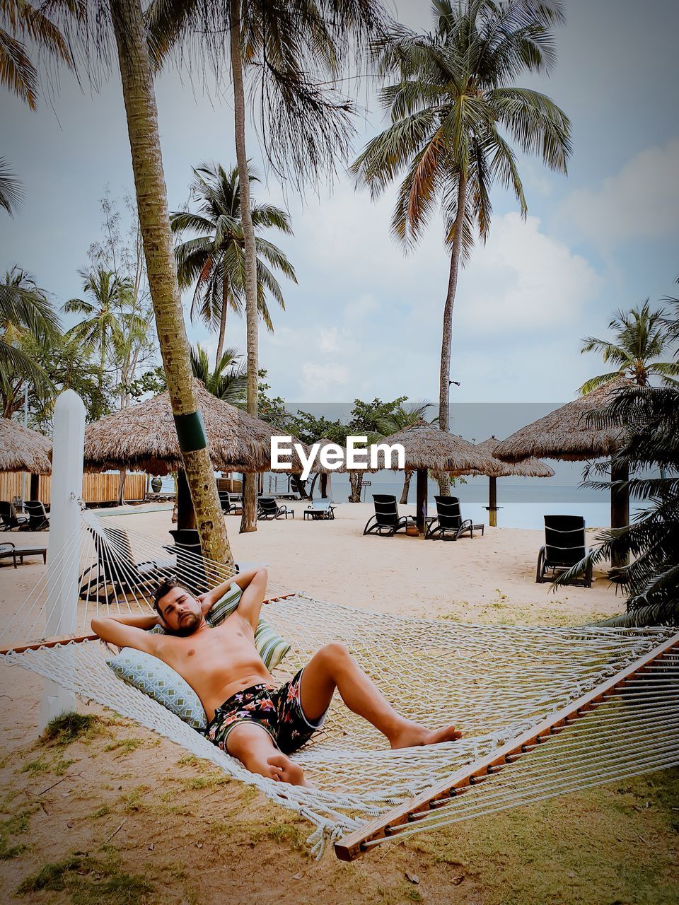 Full length of shirtless man relaxing in hammock on beach