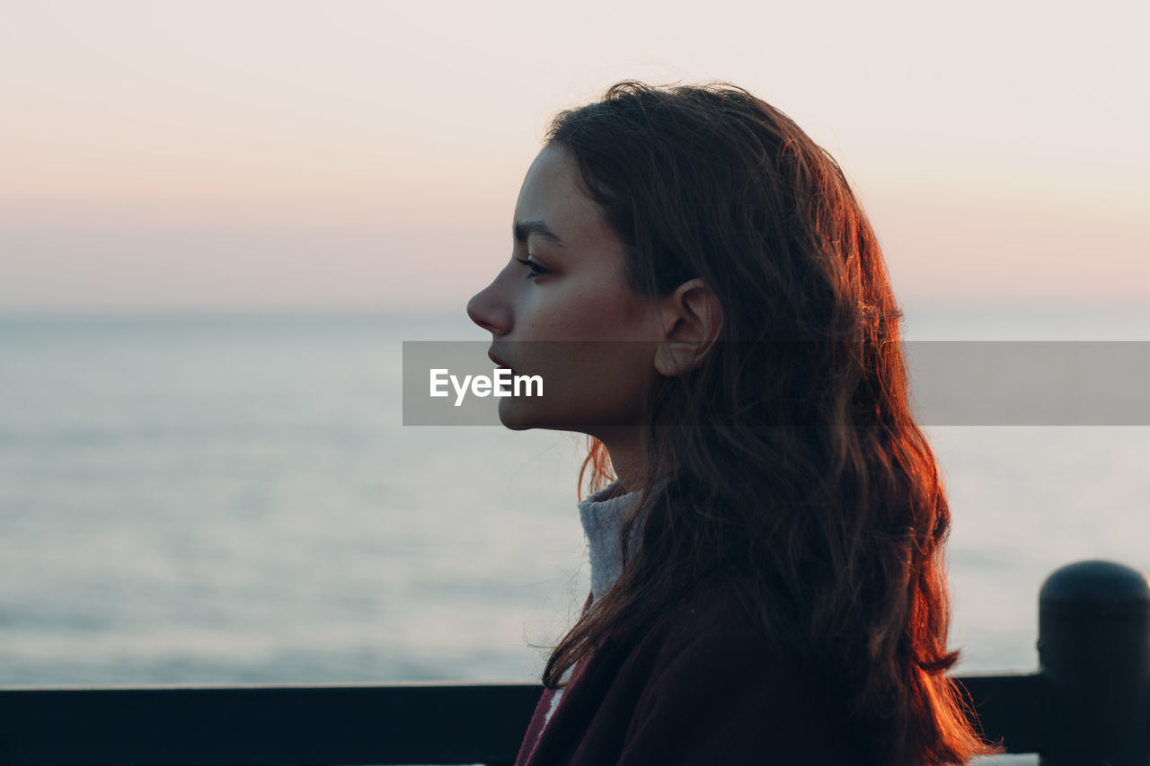 PORTRAIT OF BEAUTIFUL WOMAN LOOKING AWAY AGAINST SEA