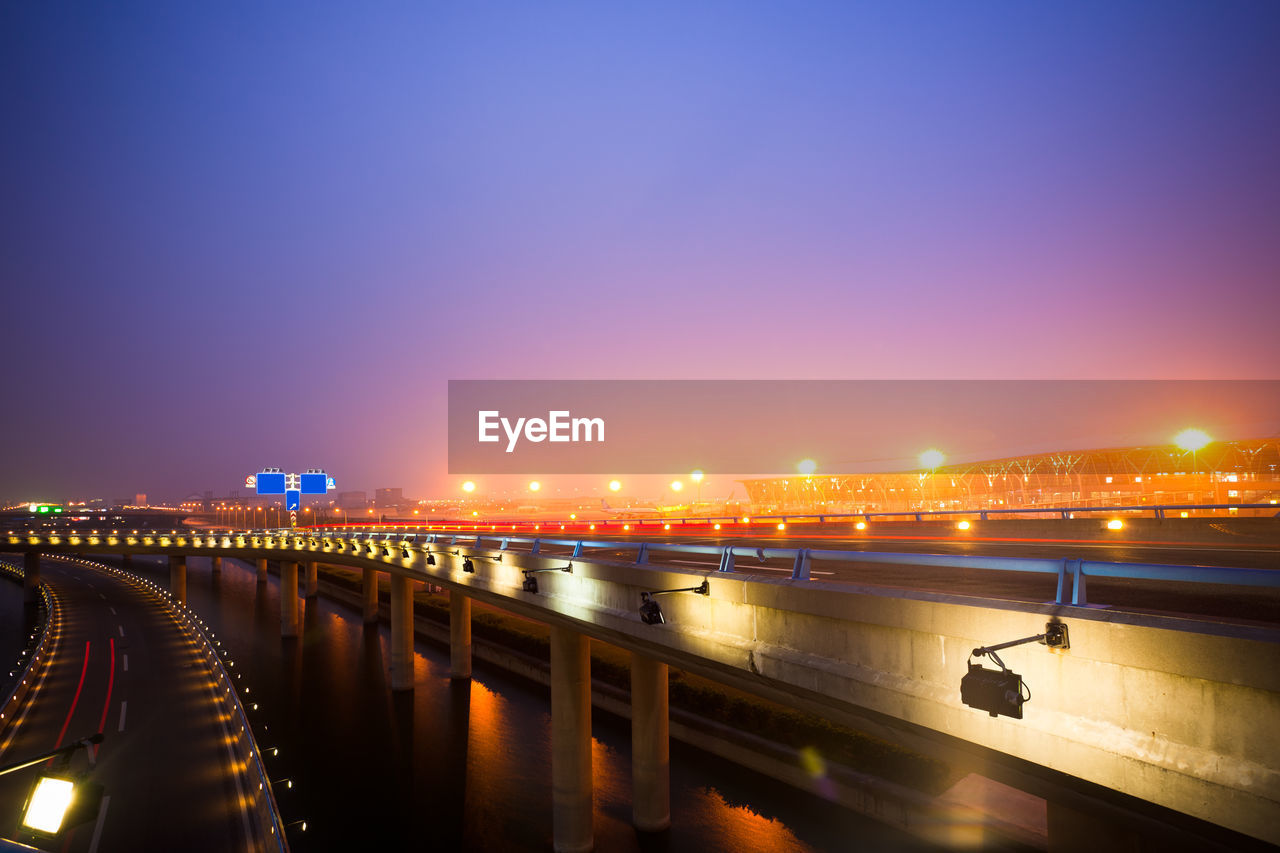 ILLUMINATED BRIDGE OVER RIVER IN CITY AGAINST CLEAR SKY