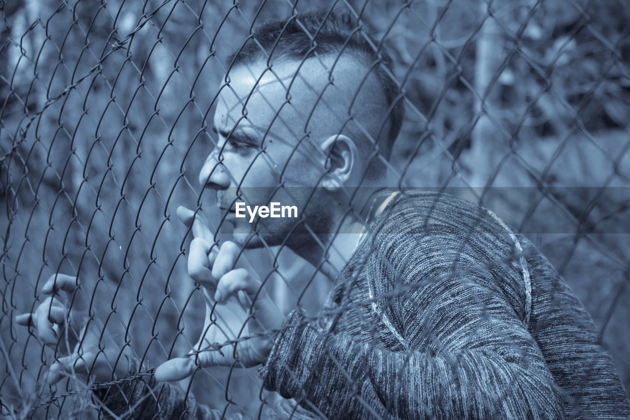 Young man looking through chainlink fence