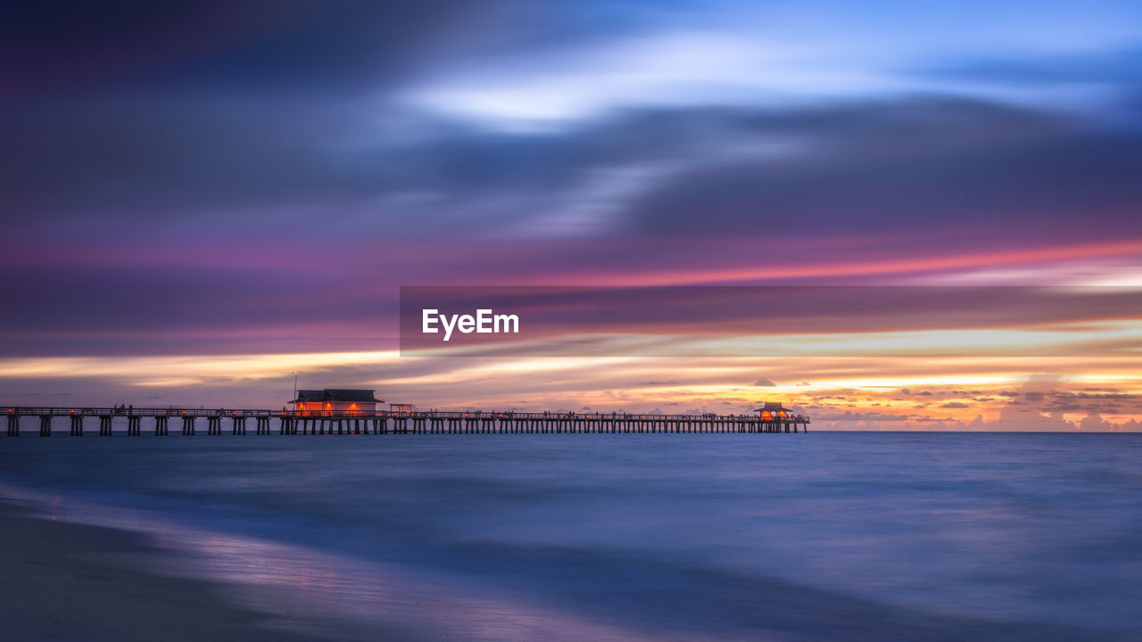 Pier over sea against dramatic sky during sunset