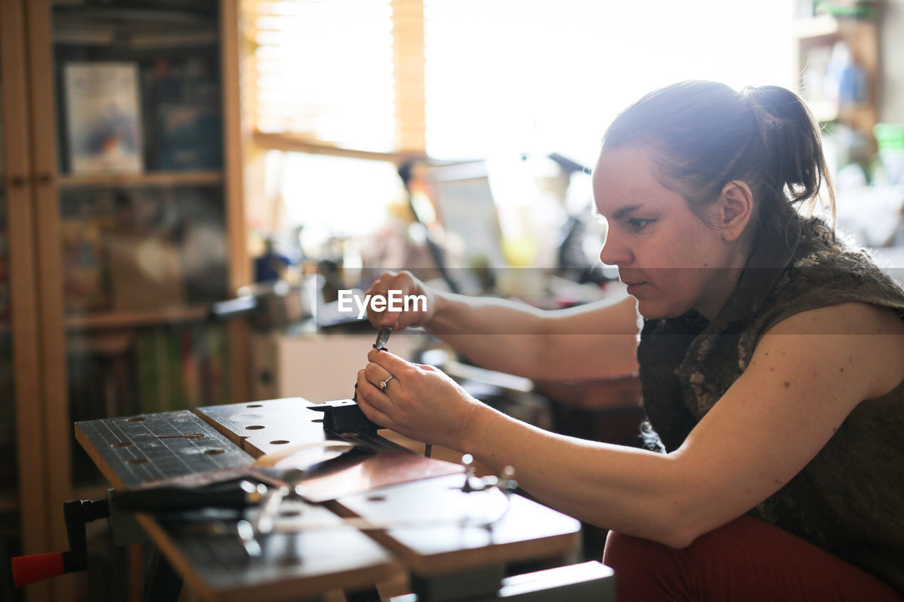 Girl master processes the metal copper plate on the workbench in the home workshop, soft focus 