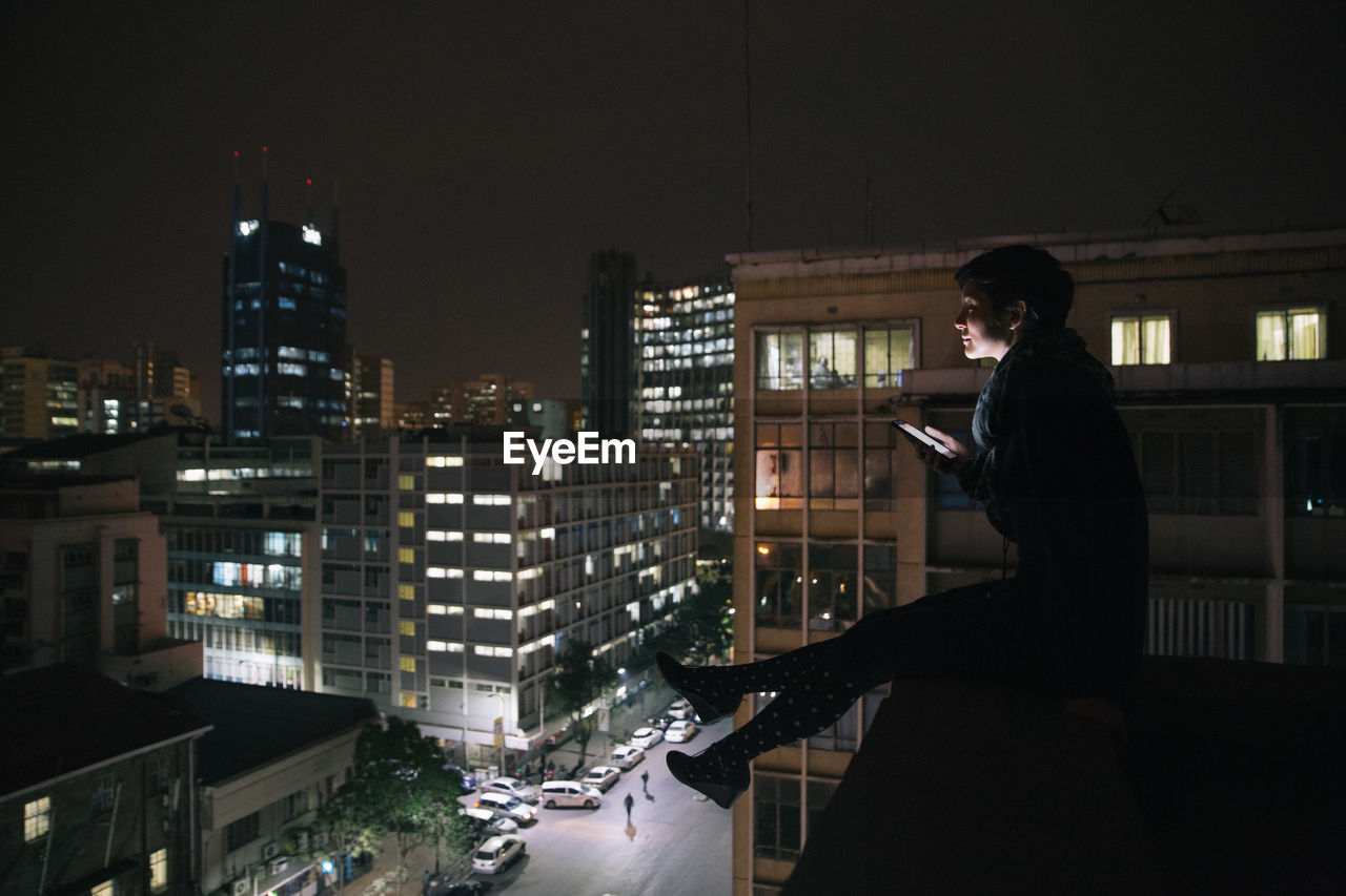 WOMAN STANDING IN ILLUMINATED CITY