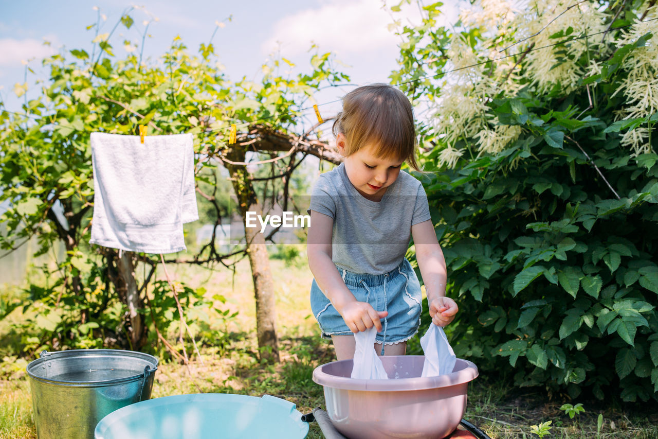 Little preschool girl helps with laundry. child washes clothes in garden