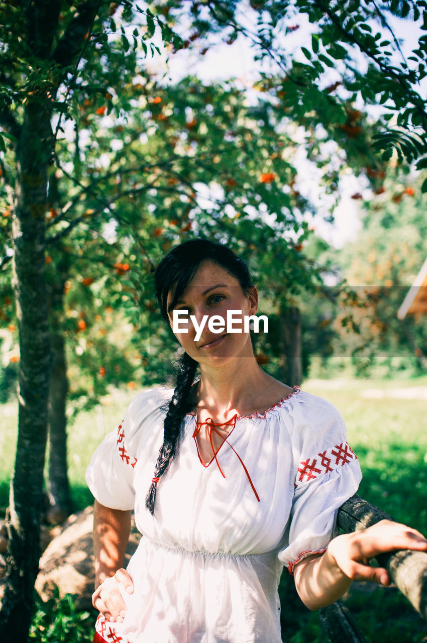 Portrait of beautiful woman standing on field against trees