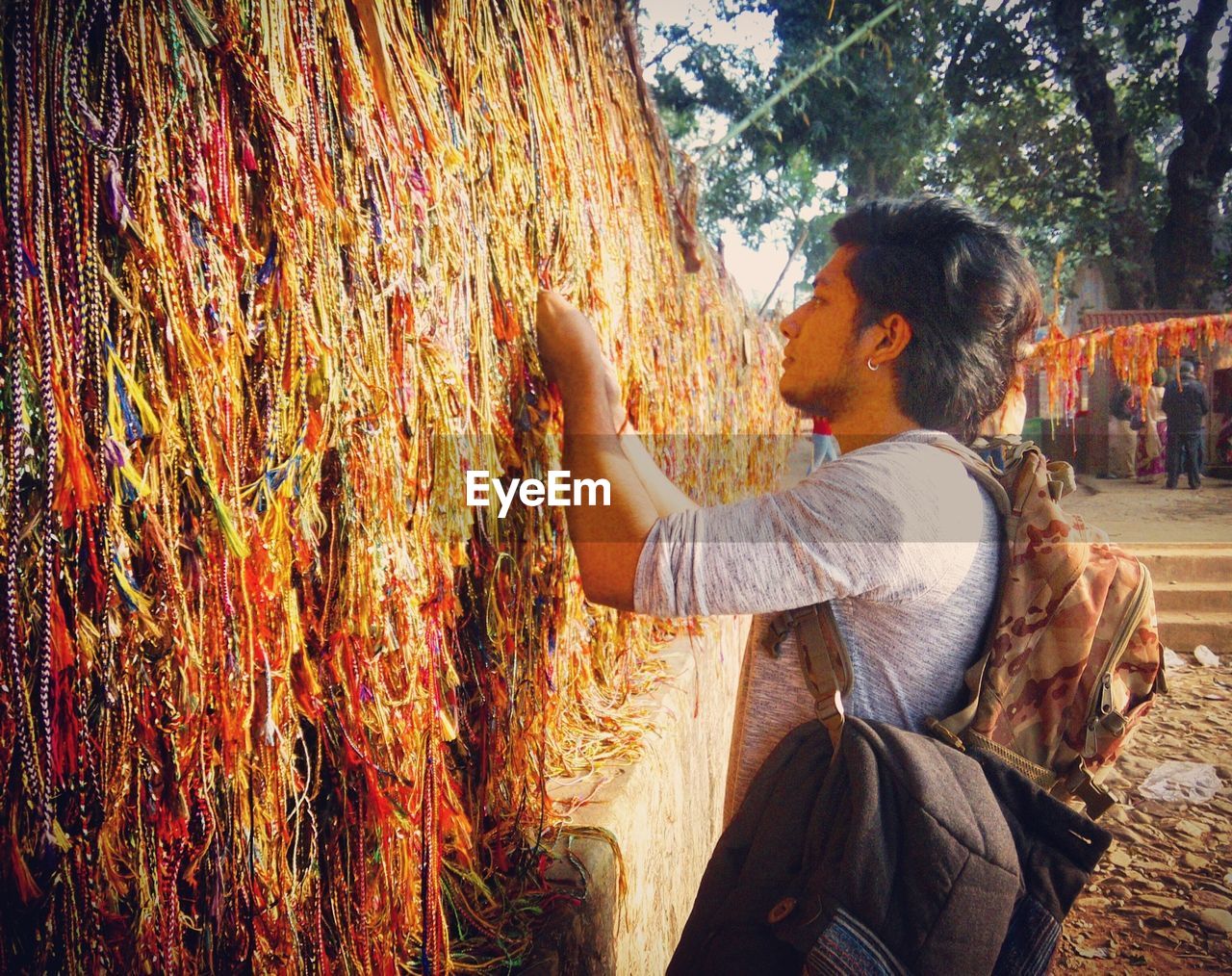 Side view of man tying prayer beads on wall at temple