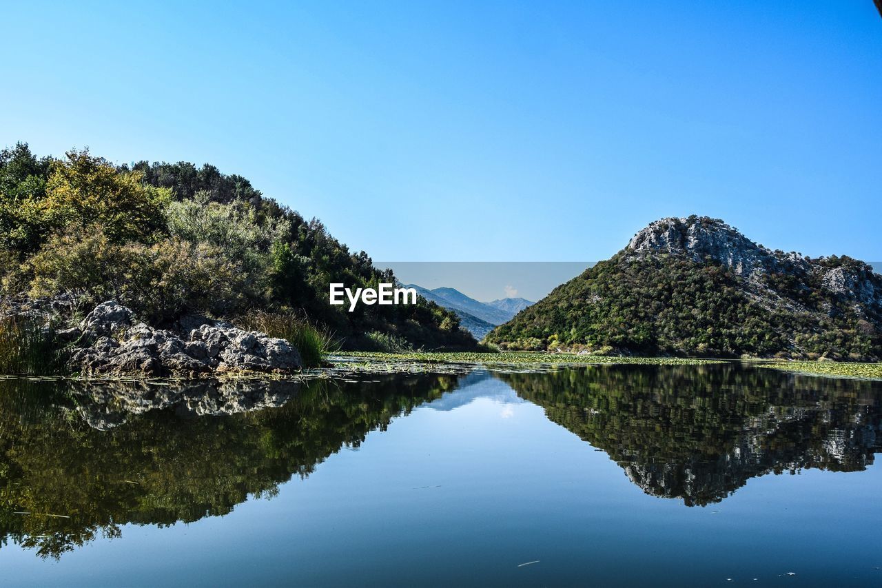 Scenic view of lake by trees against clear blue sky