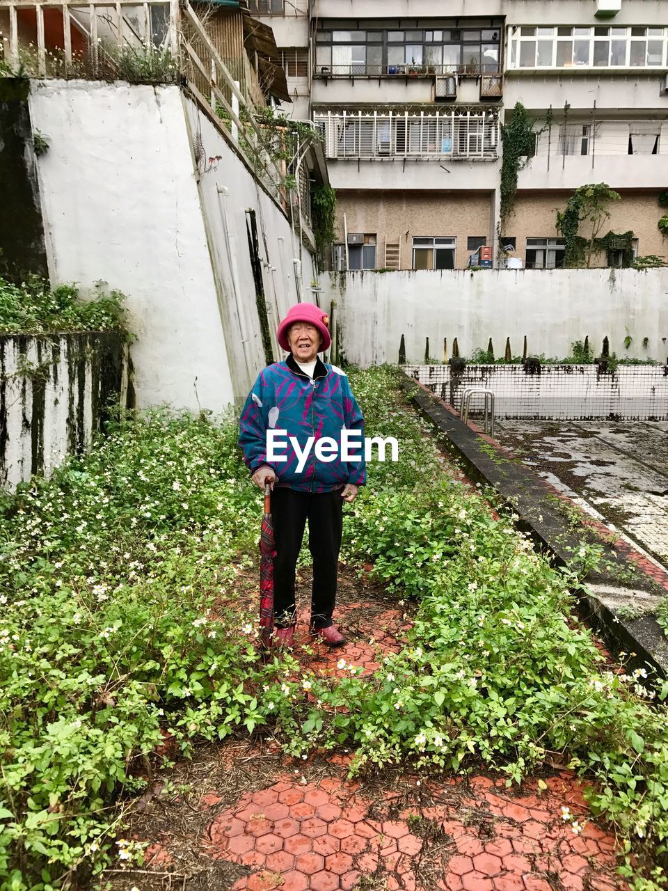 Senior woman standing by plants against building