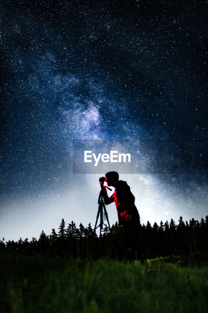 Silhouette man photographing on land against sky at night