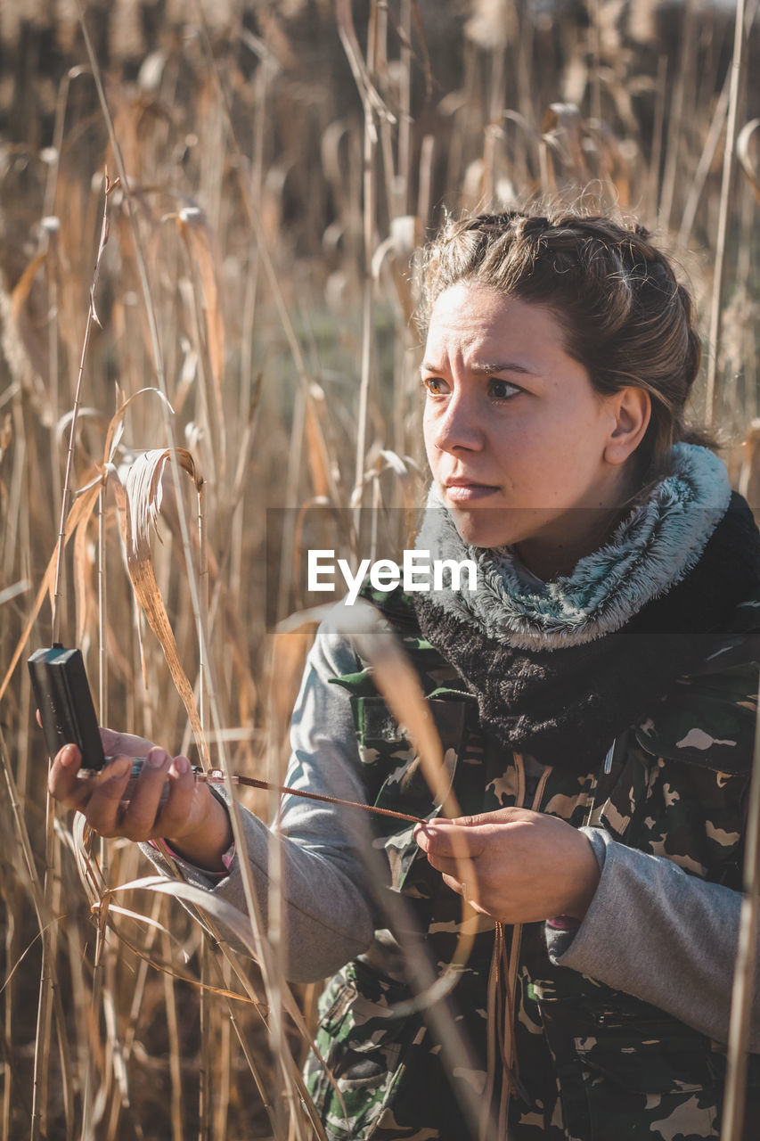 Woman holding mirror compass standing amidst field in forest