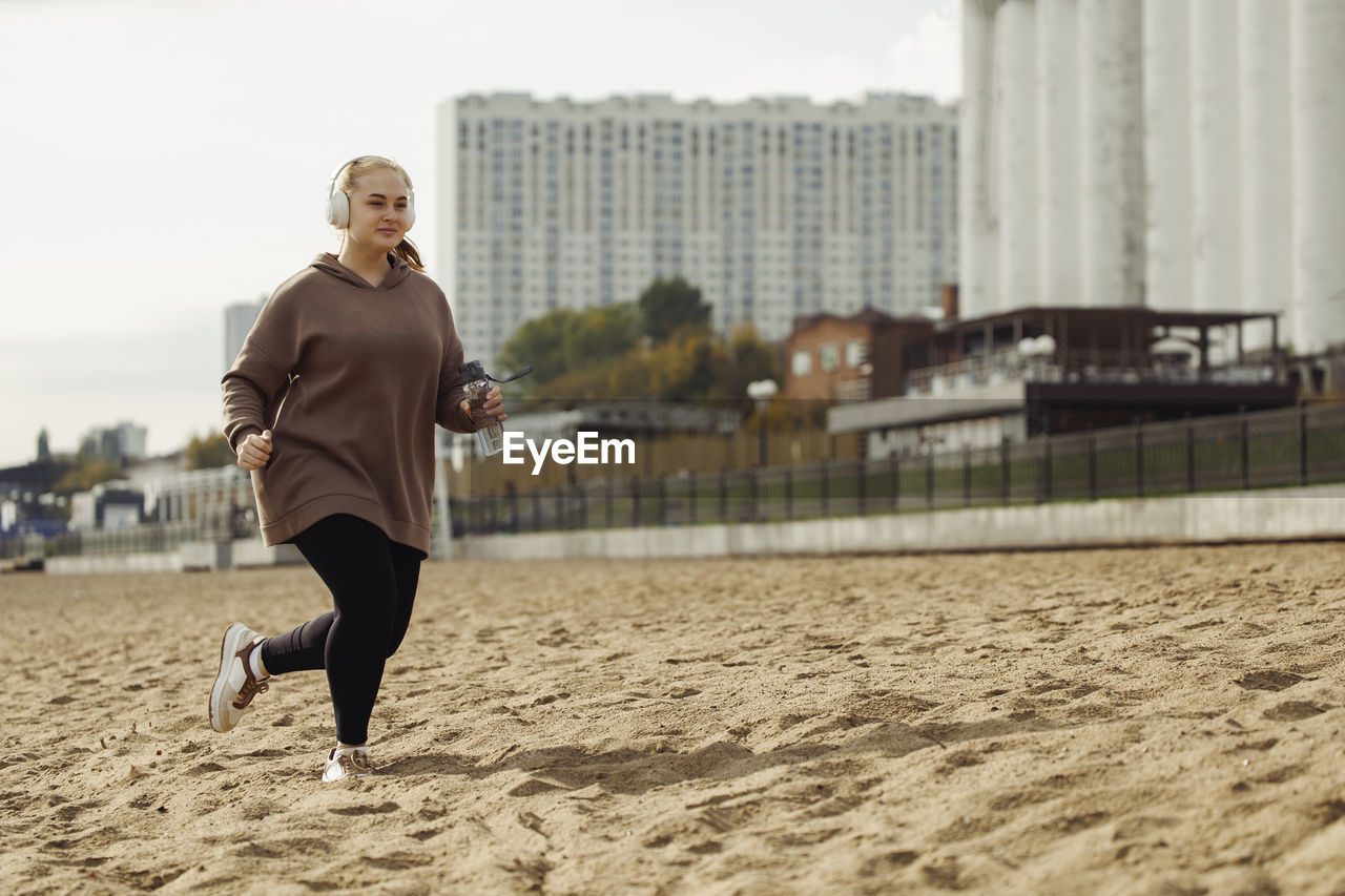 Young woman wearing headphones running at sandy beach