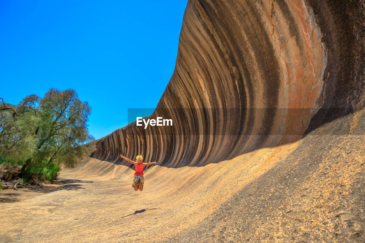 Woman with arms outstretched jumping by cliff